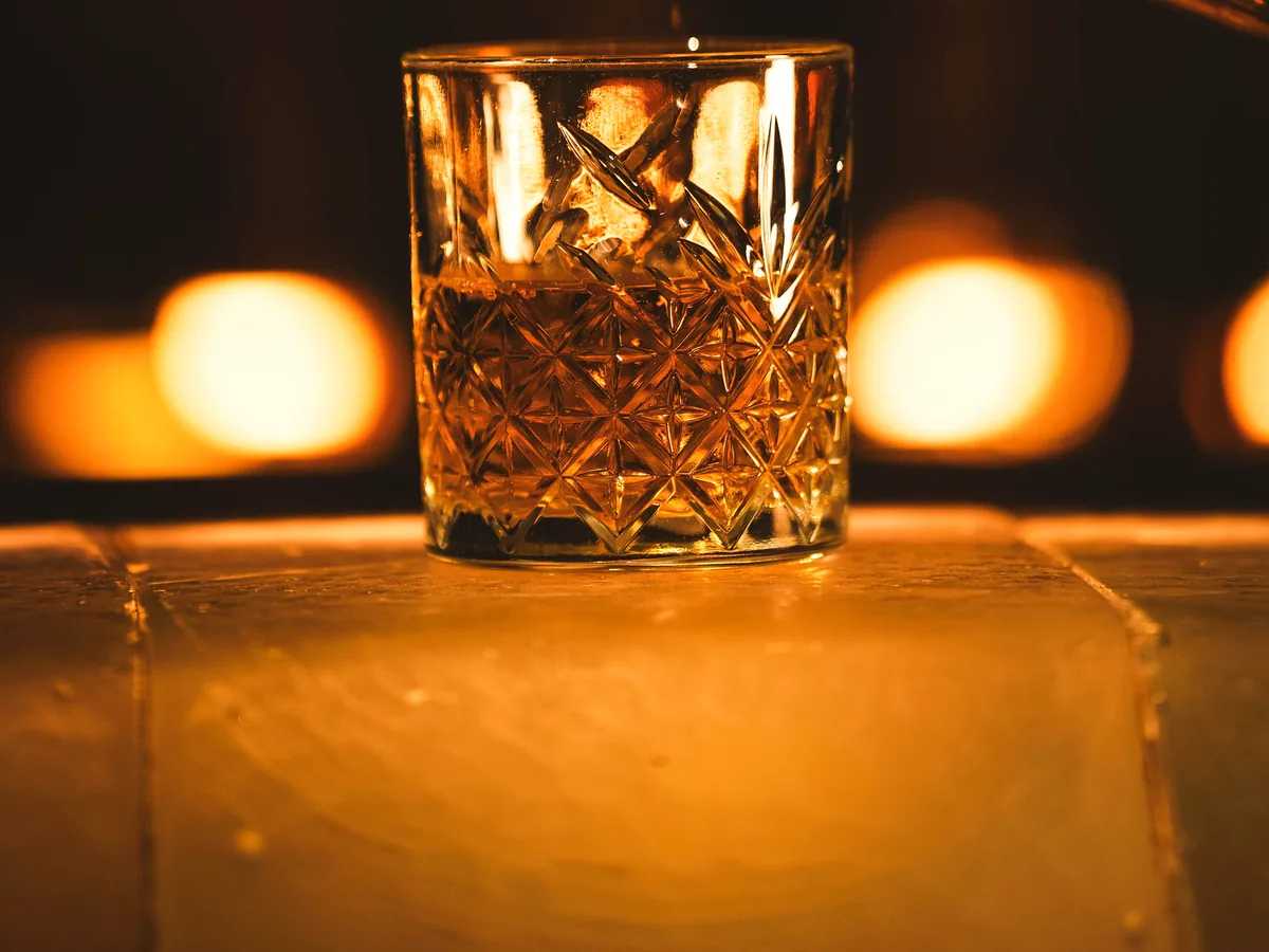 A drink in a cut-glass tumbler on the bar, tealights burning behind it