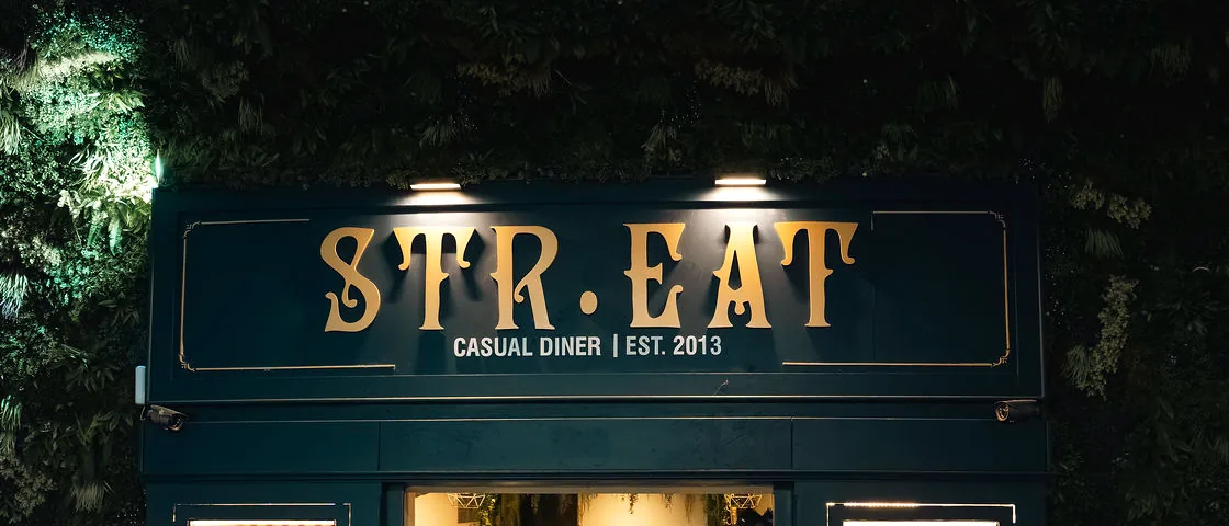 The STR·EAT sign lit above the entrance at night, gold lettering on navy