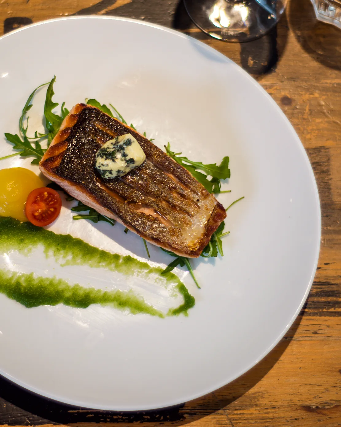 A fillet of Mediterranean sea bass, crisp skinned, with rocket and tomatoes on a white plate