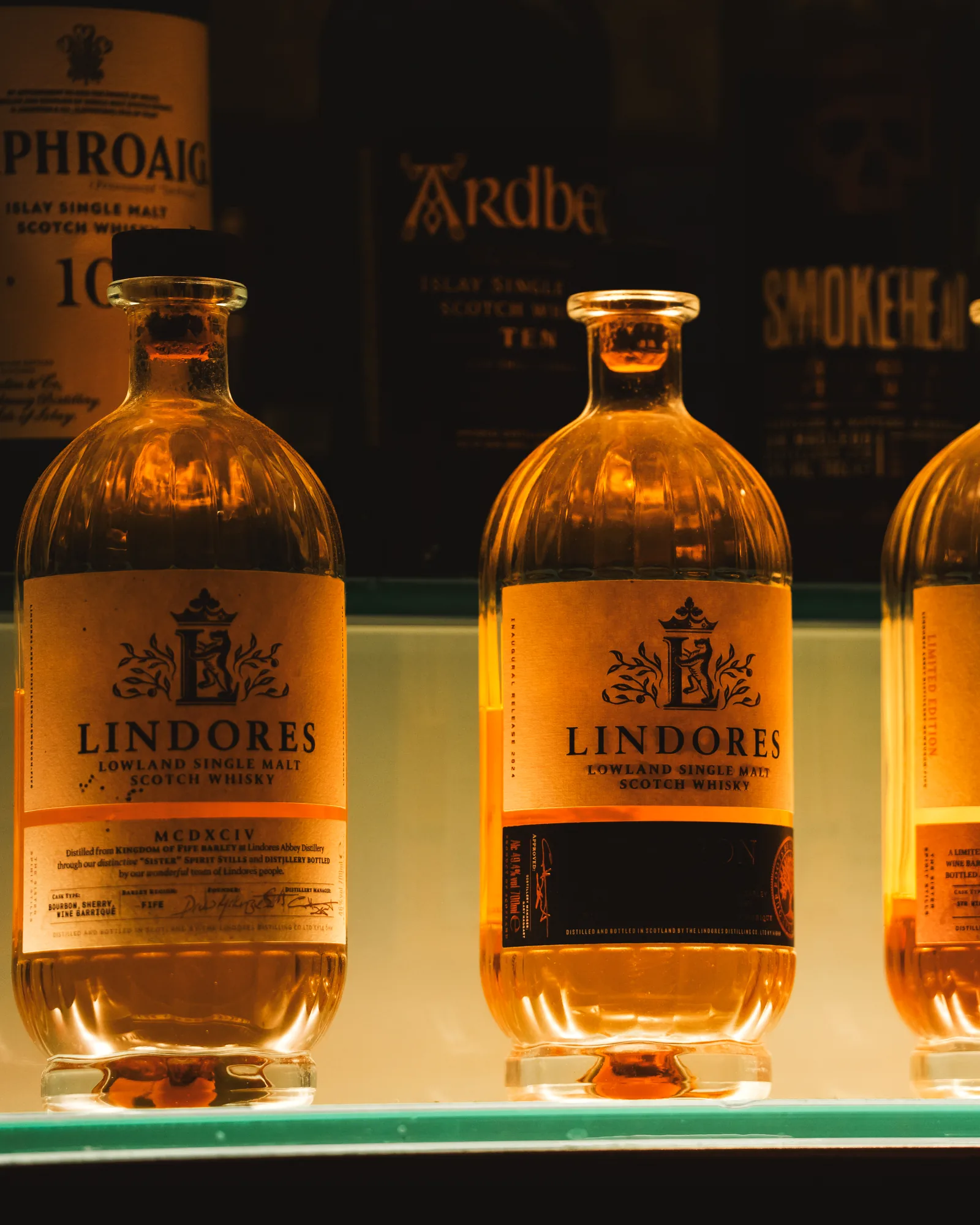 Bottles of Lindores Abbey Lowland single malt on a lit shelf at STR·EAT, Laphroaig and Ardbeg behind
