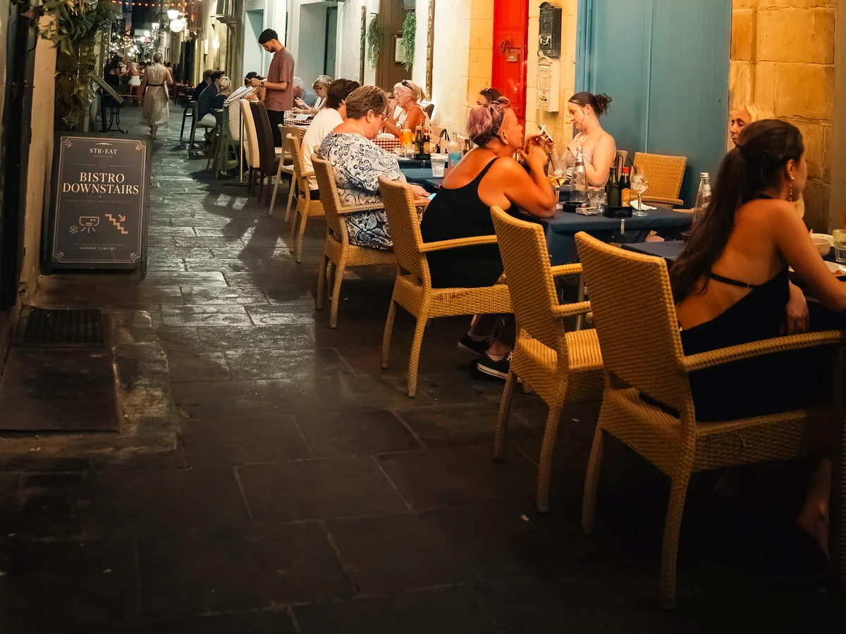 Tables out on Strait Street at night, lit warm along the alley
